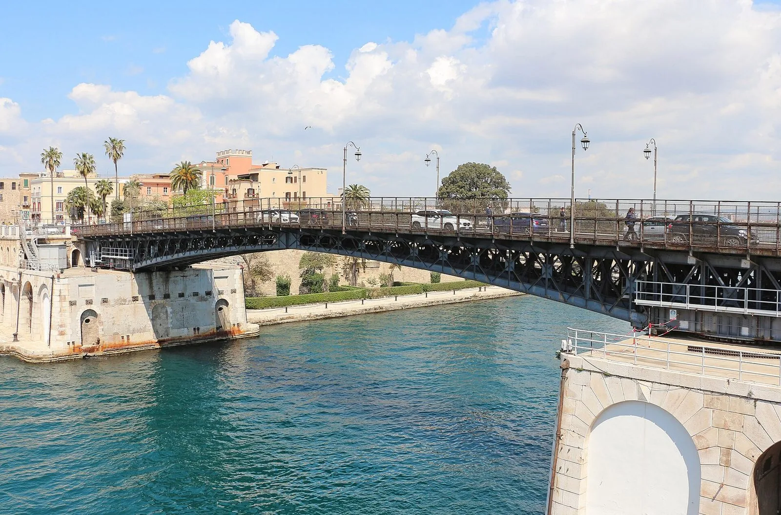 Il ponte girevole di Taranto in ferro sul canale navigabile, con l'acqua turchese, le palme e i palazzi della città sullo sfondo