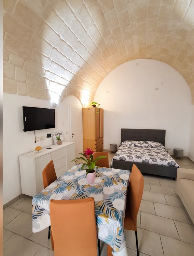 La volta a botte in pietra sopra la zona notte, con il letto matrimoniale, la TV a parete e il tavolo da pranzo