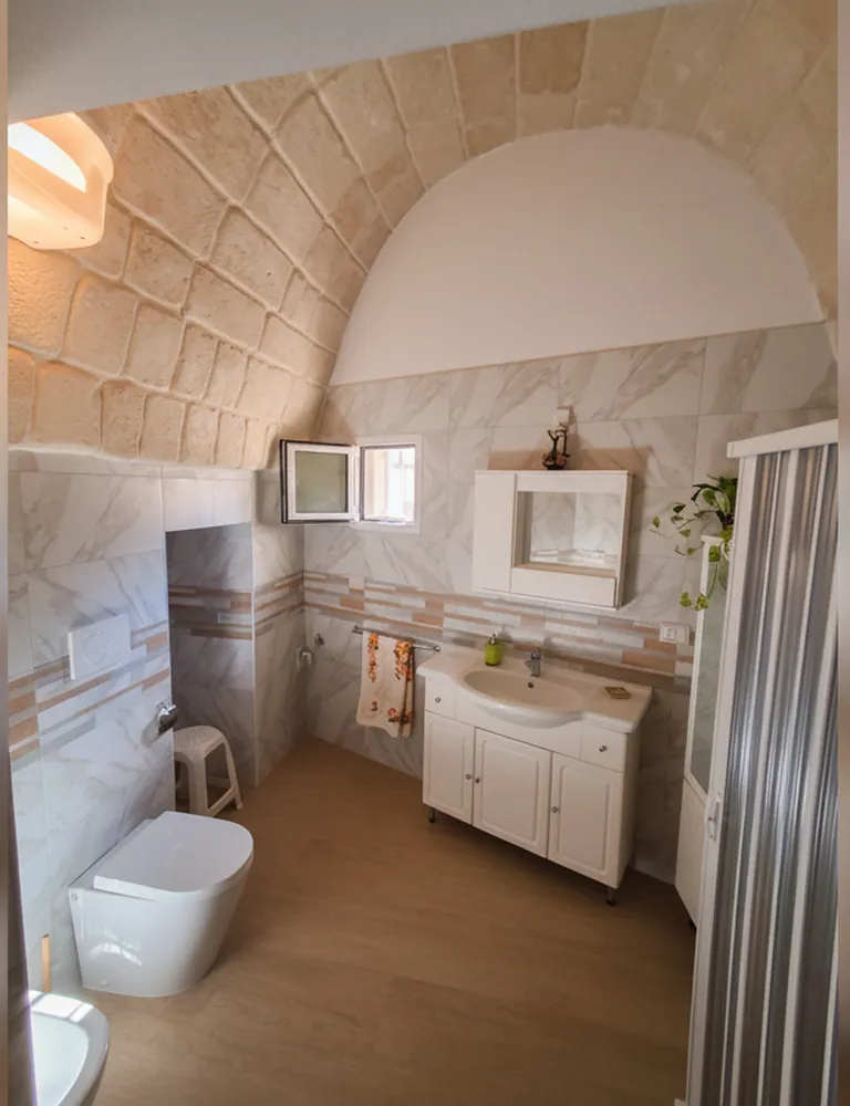 Il bagno privato sotto la volta in pietra, con il lavabo, lo specchio, i sanitari e il box doccia